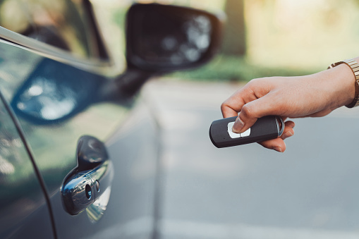 Close up hands woman pressing remote systems key near car for lock,unlock of blue hatchback car near street road driving.