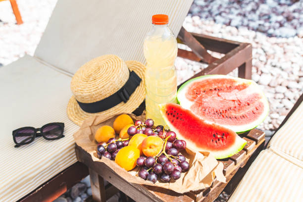 pique-niquer à la plage. fruits frais sur la table près des chaises longues - beach table peach fruit photos et images de collection
