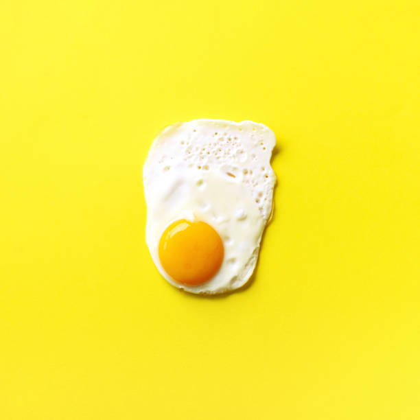 istock One fried egg on yellow paper background. Creative food concept in minimal style. Top view 1152147142