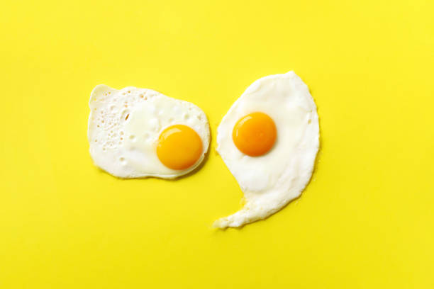 istock Two fried eggs on yellow paper background. Creative food concept in minimal style. Top view 1152147165