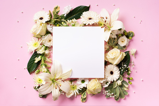 Creative layout with white flowers, square shape paper for copyspace over pink background. Top view, flat lay. Spring and summer concept