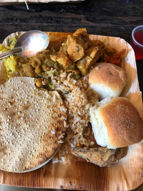 Stock photo showing Indian buffet food platter, lemon rice and boled / steamed rice, Indian cuisine chicken tikka masala curry with gravy, spiced fried fish, fresh bread rolls, pepper and cabbage sabji / subji / sabzi square bamboo plate with spoon, curry and rice imagen de plato de comida buffet indio, arroz con limón y arroz en negrita/al vapor, cocina india pollo tikka masala curry con salsa de carne, pescado frito con especias, panecillos frescos, pimienta y col sabji/subji/sabzi placa de bambú cuadrado con cu