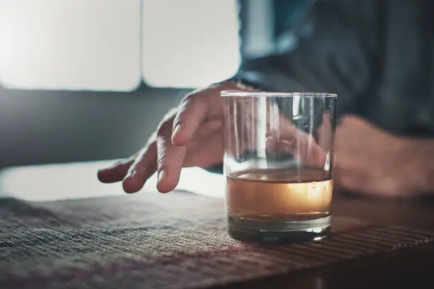 A man's hands reach out to take a glass containing liquor of some kind.