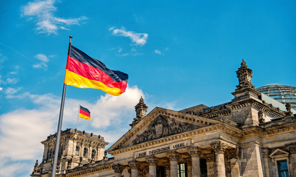 Deutsche Flaggen wehen im Wind am berühmten Reichstagsgebäude, Sitz des Deutschen Bundestages, an einem sonnigen Tag mit blauem Himmel und Wolken, Zentralbezirk Berlin Mitte, Deutschland