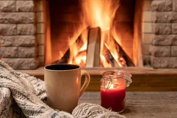 Photo of Big mug with hot tea, and a candle , wool scarf, near cozy fireplace, hygge, home sweet home.