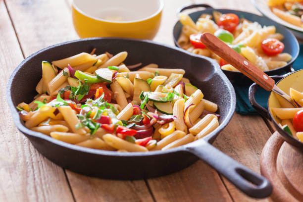 Penne pasta prepared with vegetables and parmesan cheese served in metal plate, close-up