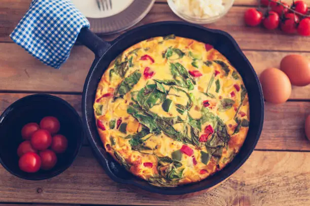 Tasty breakfast, frittata with Baby spinach, bell peppers goat cheese, and cherry tomatoes grated in oven in cast iron pan, close-up,