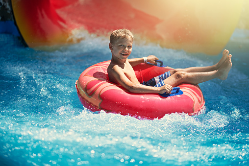 Little boy enjoying water slide in waterpark. The boy has slid using inflatable tube.\nNote: the tube and slide colors adjusted and text removed in post processing.\nNikon D850