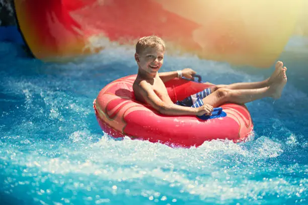 Little boy enjoying water slide in waterpark. The boy has slid using inflatable tube.
Note: the tube and slide colors adjusted and text removed in post processing.
Nikon D850