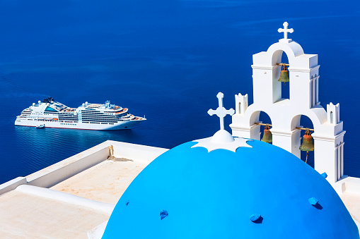 Oia, Santorini, Greece - April 25, 2019: Iconic view of blue and white church dome and bell tower, sea and cruise ship