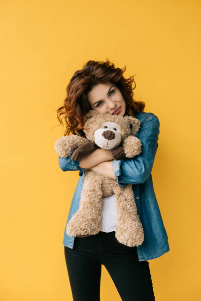 istock pretty redhead girl hugging teddy bear and looking at camera on orange 1152171734
