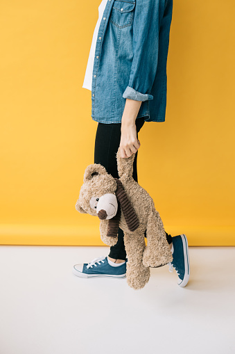 cropped view of young woman holding teddy bear on orange