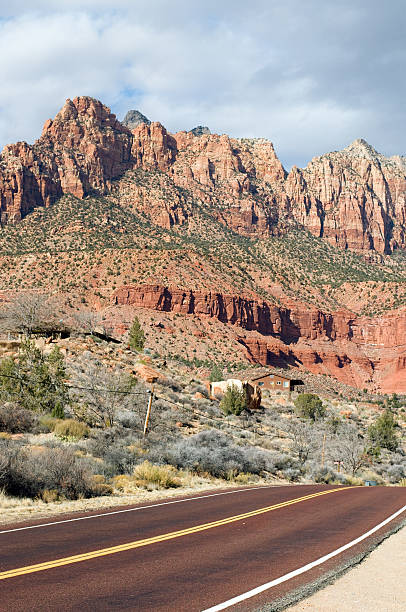 Asphalt Mountain Road A flat two-lane highway making a sudden slope by a humble settlement in a rocky area. Shot from the roadside. single yellow line sunlight usa utah stock pictures, royalty-free photos & images