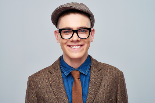 Portrait of cheerful young man wearing old-fashioned suit with cap and glasses smiling at camera