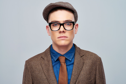 Portrait of serious young man wearing trendy brown jacket with glasses and cap