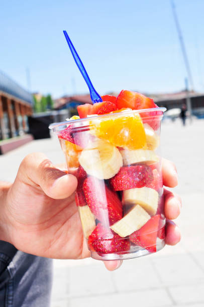 closeup of a young caucasian man eating a fruit salad in a clear plastic cup outdoors