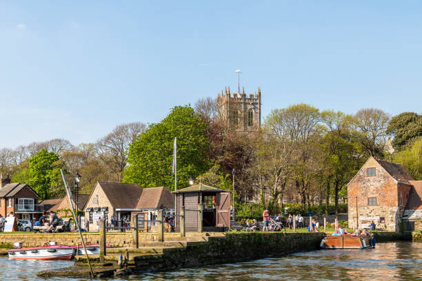 Christchurch Quay with Priory in background Christchurch, UK - April 21 2019: Christchurch Quay with Priory in the background, people on a boat and on the quayside. christchurch england photos stock pictures, royalty-free photos & images