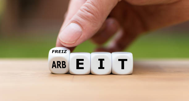 hand turns a dice and changes the german word "arbeit" ("work" in english) to "freizeit" ("leisure time" in english). - arbeit imagens e fotografias de stock