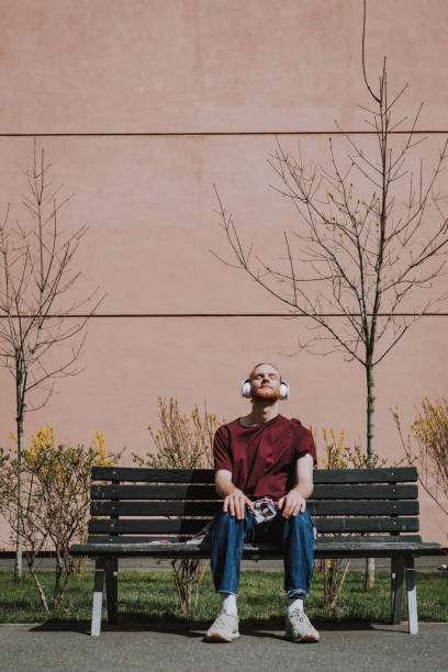 istock Red haired hipster man enjoying music on bench 1152185415