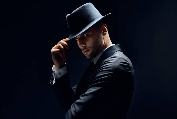 istock Young handsome man in black suit touch his hat on dark background 1152186184