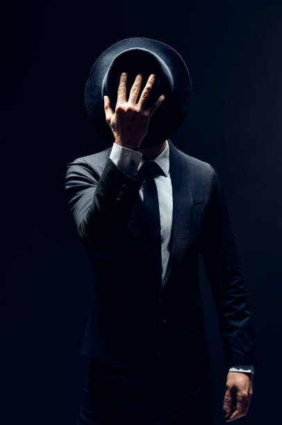 istock Man in suit hiding face behind his hat isolated on dark background 1152186191