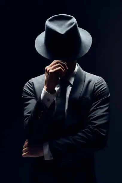 Man in suit hiding face behind his hat isolated on dark background. secret and incognito concept