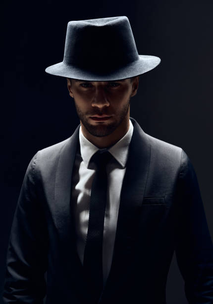 istock Handsome confident man in black suit and hat on dark background 1152186208