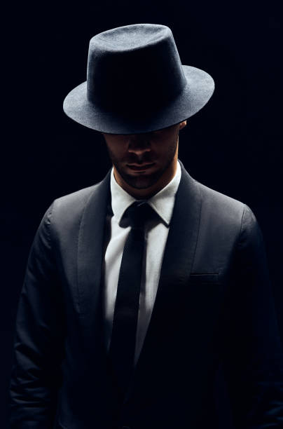 istock Handsome confident man in black suit and hat on dark background 1152186264