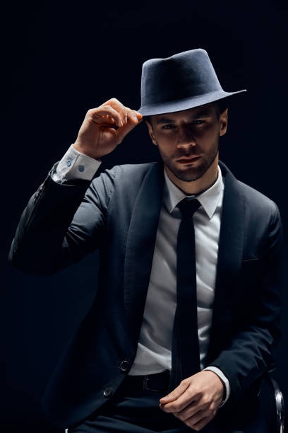 istock Young handsome man in black suit touch his hat on dark background 1152186379
