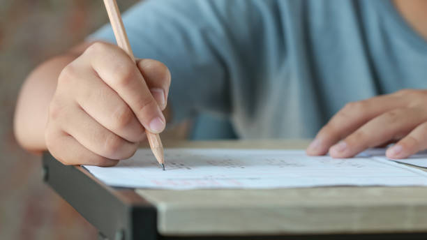 istock Exam test school or university concept : Hand student holding pencil writing standardized answer multiple carbon paper form with gray black answers sheet bubbled doing final assessment in classroom 1152187821