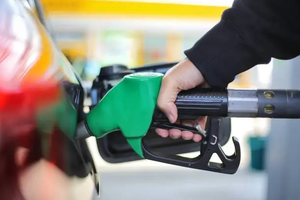 Close up hand holding green gasoline fuel nozzle and being fill gas tank of black car in gas station Concept of Global Fossil Fuel Consumption Replace by alternative energy in near the near future