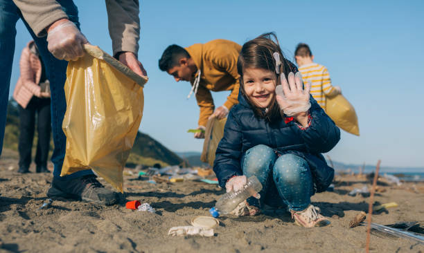 Volunteers cleaning the beach Little happy girl with volunteers picking up trash on the beach microplastic photos stock pictures, royalty-free photos & images