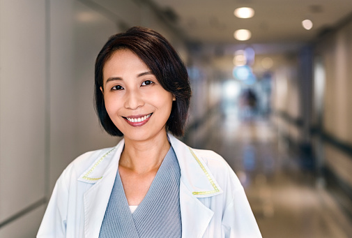 Portrait of smiling medical expert wearing lab coat. Beautiful mid adult healthcare worker is in corridor. She is a doctor working in hospital.