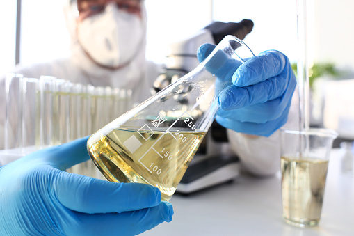 Scientist arm in protective gloves hold yellow liquid in bottle closeup