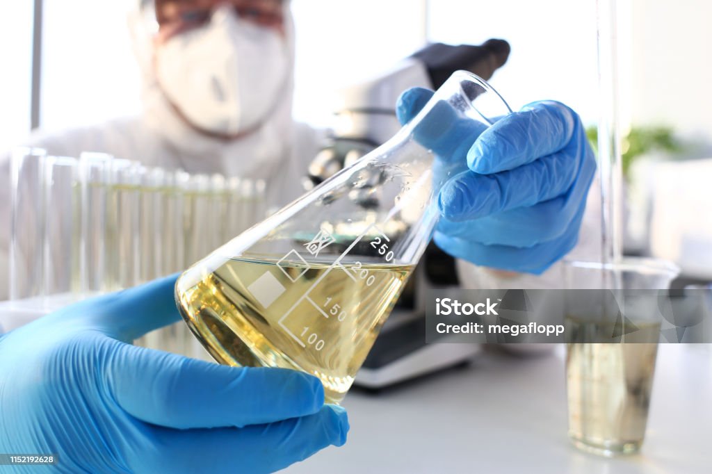 Scientist arm in protective gloves hold yellow liquid in bottle Scientist arm in protective gloves hold yellow liquid in bottle closeup Chemical Stock Photo