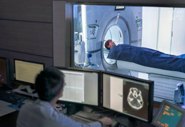 Doctor examining scan while patient in MRI scanner Doctor examining scan on computer while patient entering in MRI scanner. Medical expert and woman are in medical examination room. They are in hospital. radiologist photos stock pictures, royalty-free photos & images