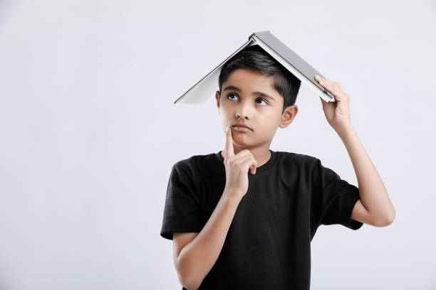 маленький индийский / азиатский мальчик с книгой на голове - reading and writing little boys reading asian ethnicity стоковые фото и изображения