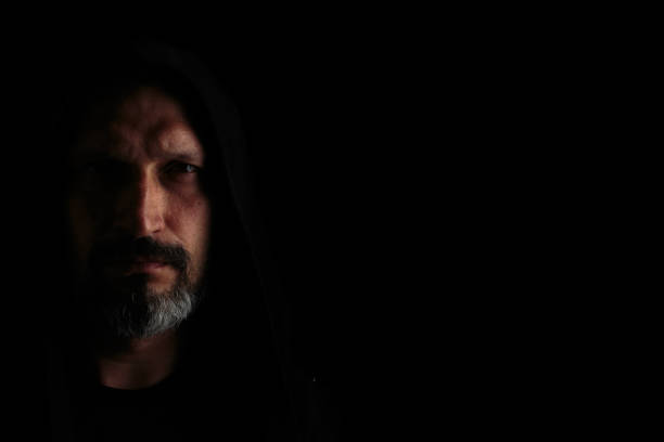 istock Brutal man with a gray beard in the hood with sharp shadows on a black background. Copy space. 1152196303