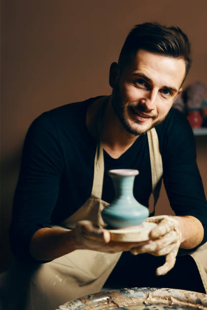 istock Smiling handsome man showing handmade ceramic pot at pottery workshop 1152196570