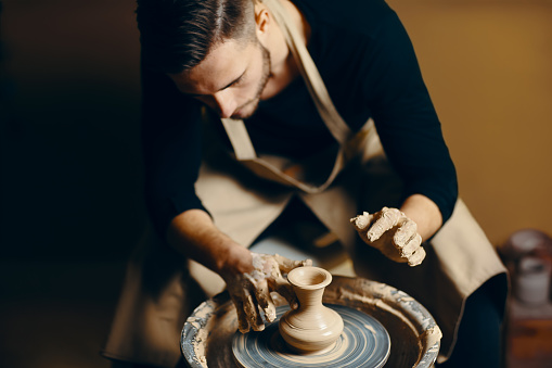 Man potter working on potters wheel making ceramic pot from clay in pottery workshop