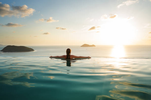 девушка в бассейне на закате с видом на горы и море - poolside enjoyment sensuality blue стоковые фото и изображения