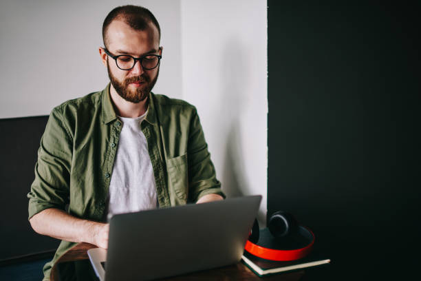 istock Handsome IT developer in casual wear and eyeglasses using laptop at cafe professional typing some serious stuff to new netbook, hipster guy searching lessons of online courses about programming 1152207109