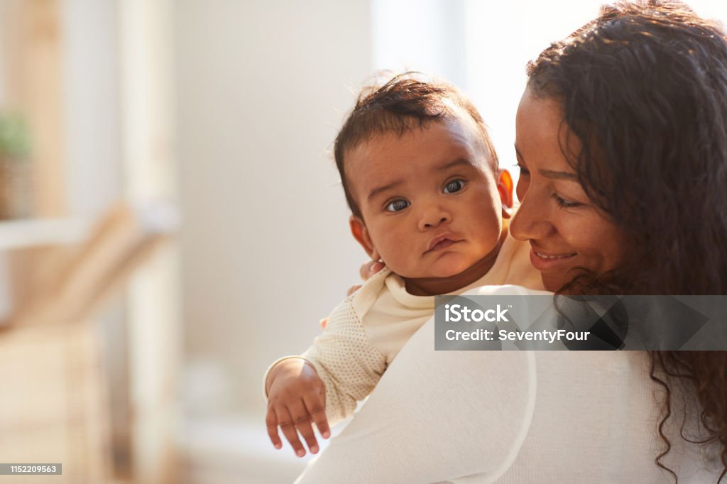 Smiling African mom holding baby Smiling loving young African mom with curly hair standing in room and holding adorable baby boy with chubby cheeks Baby - Human Age Stock Photo