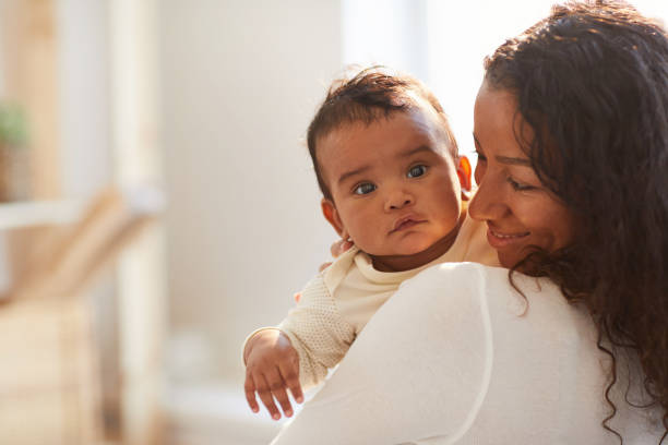 Smiling African mom holding baby Smiling loving young African mom with curly hair standing in room and holding adorable baby boy with chubby cheeks mother and baby stock pictures, royalty-free photos & images