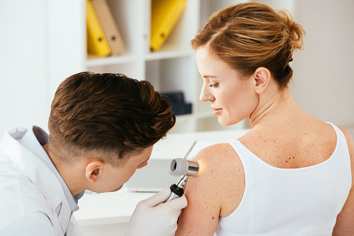 dermatólogo en guantes de látex que sostienen dermatoscopio mientras examina a un paciente atractivo con enfermedad cutánea photo