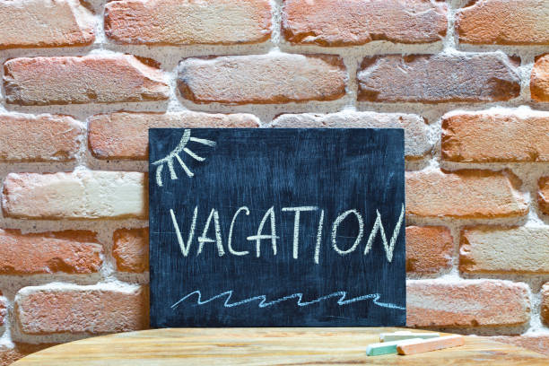 istock Chalk board with the word VACATION drown by hand and chalks on wooden table on brick wall background. 1152217795