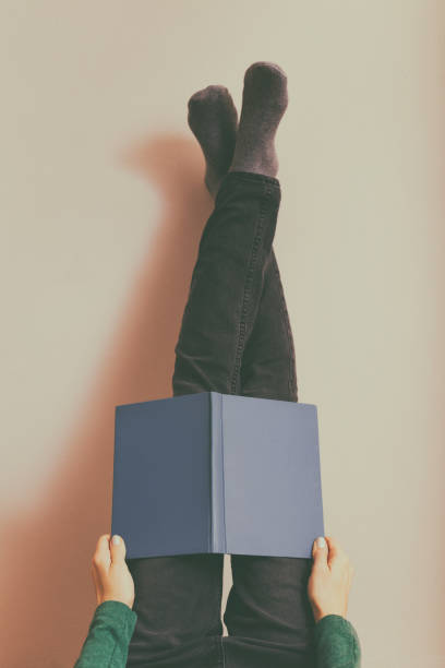 Woman resting and reading book with legs up in front of the wall.Toned photo.