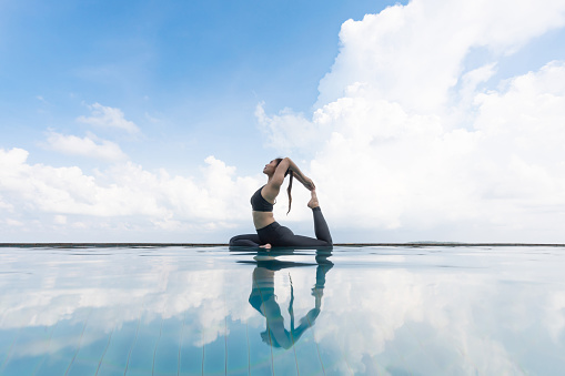 Vacation of Attractive Asian woman relaxing in yoga king pigeon pose on the pool above the beach with beautiful sea in Tropical island,Feeling comfortable and relax in holiday,Vacations Concept