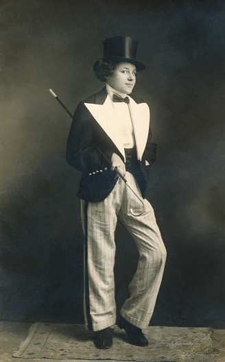 Vintage 1930s portrait of a young girl with curly hair and black top hat, holding a baton and wearing a classic black and white tap dance outfit.