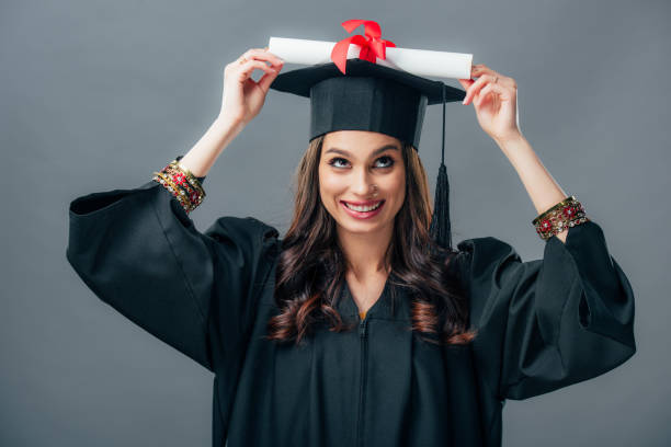 istock cheerful indian student in graduation hat holding diploma, isolated on grey 1152229482